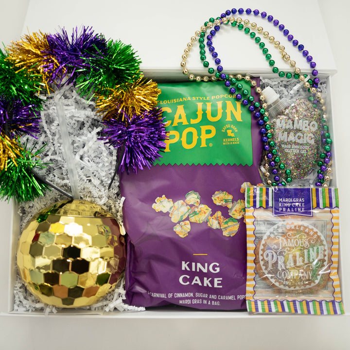 Digital photograph of a New Orleans Mardi Gras gift box featuring Cajun Pop popcorn, a gold disco ball tumbler, and vibrant purple, green, and gold tinsel and beads