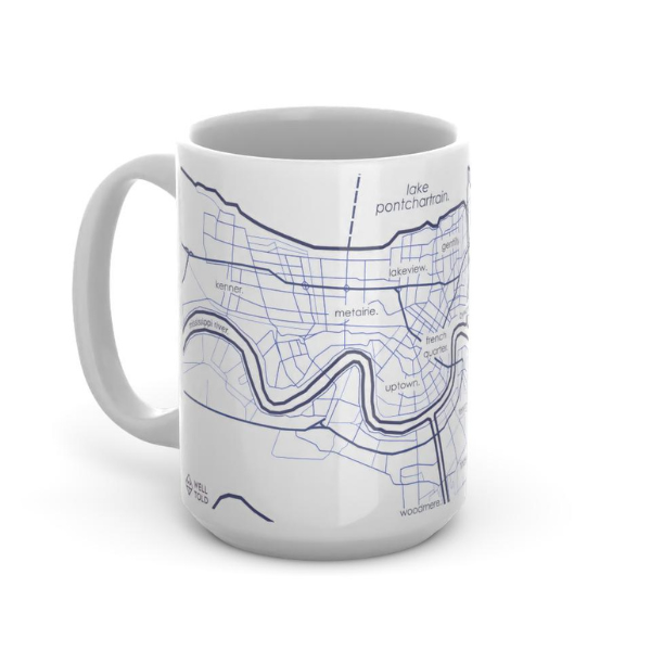 Ceramic mug by Well Told featuring a minimalist blue map of New Orleans, Louisiana, showing the winding Mississippi River, Lake Pontchartrain, and the French Quarter with fine-lined street grids and lowercase neighborhood labels on a white glossy surface