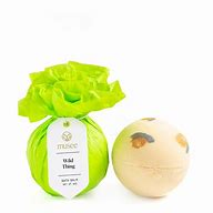 Product photography by Musee of the Wild Thing bath balm wrapped in vibrant lime green ruffled tissue paper with a white logo tag next to an unwrapped cream-colored sphere featuring orange and grey leopard spots against a white background