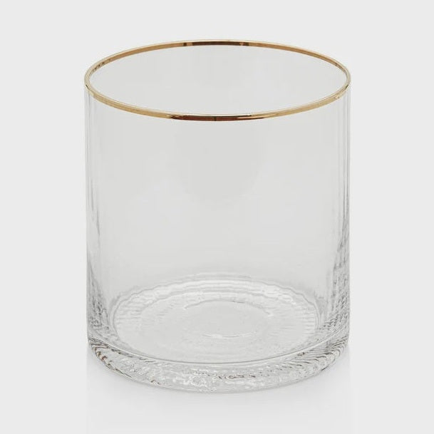 Clear glass tumbler displayed in a minimalist studio setting featuring a metallic gold-trimmed rim and a distinctive textured swirl pattern visible at the base