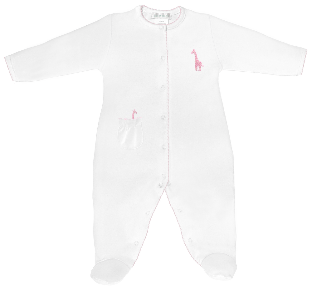 Product photograph of a Lyda Baby white footie on a white background featuring integrated feet, a pink embroidered giraffe on the chest, a ruffled pocket, and delicate pink scalloped trim along the snap-front closure