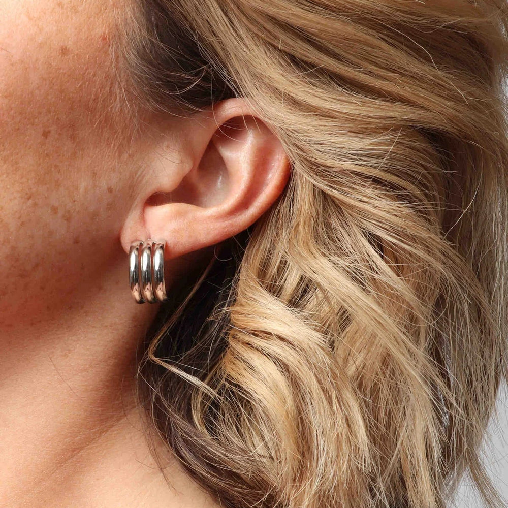 Photograph of a polished silver triple-banded hoop earring worn on a freckled earlobe framed by flowing wavy blonde hair