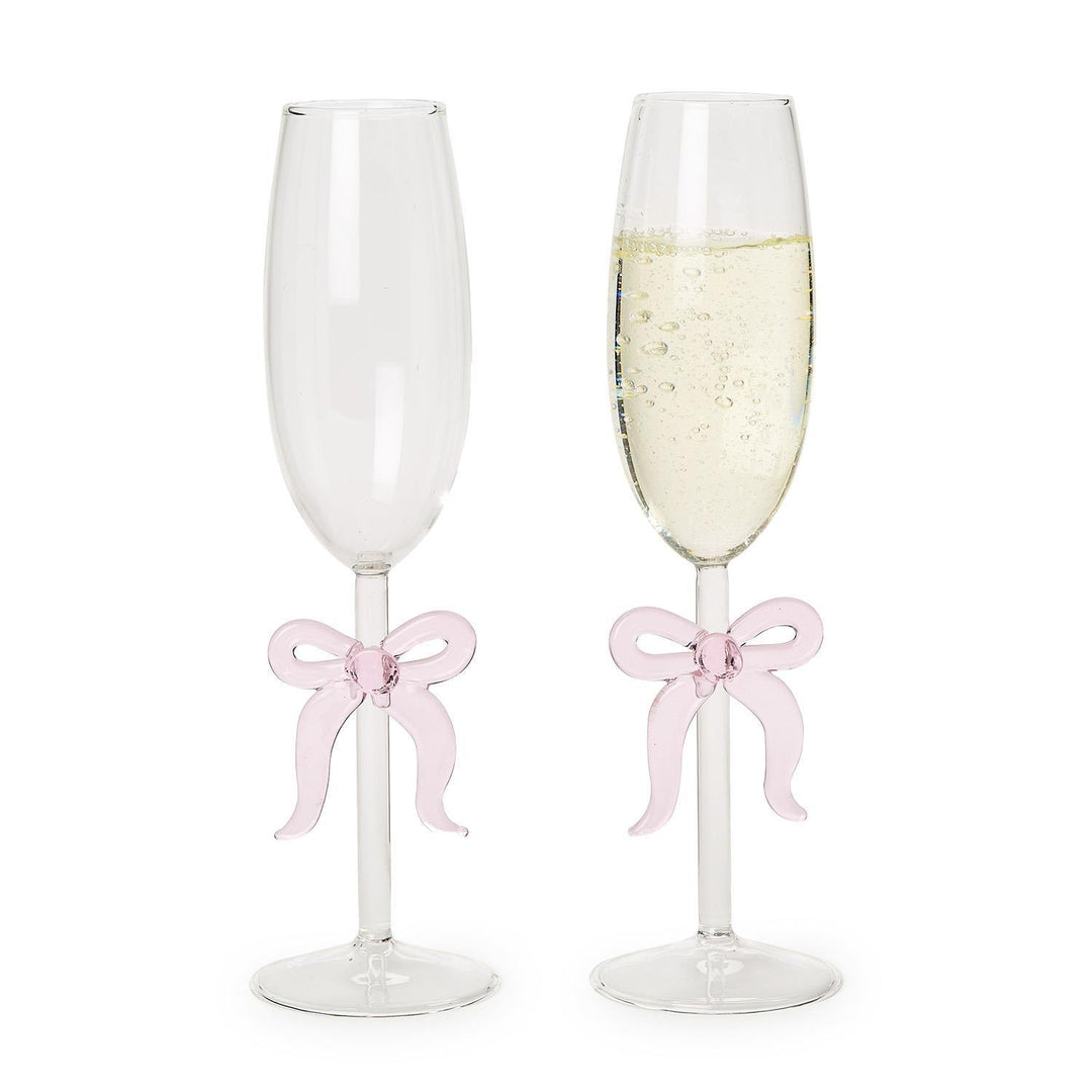 Hand-blown glass champagne flutes set against a white studio background, featuring one empty glass and one filled with effervescent sparkling wine, both uniquely adorned with decorative pink glass ribbons on their long stems