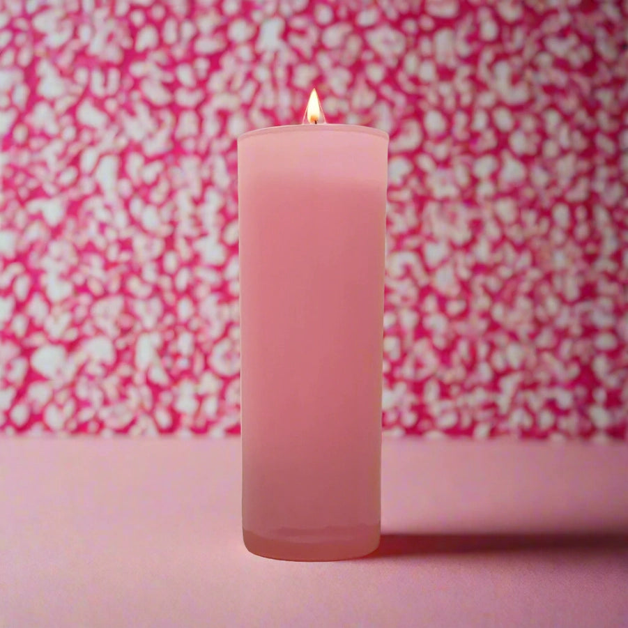 Photograph of a tall pink candle in a frosted glass holder featuring a tiny glowing flame set against a vibrant pink and white leopard-print bokeh background