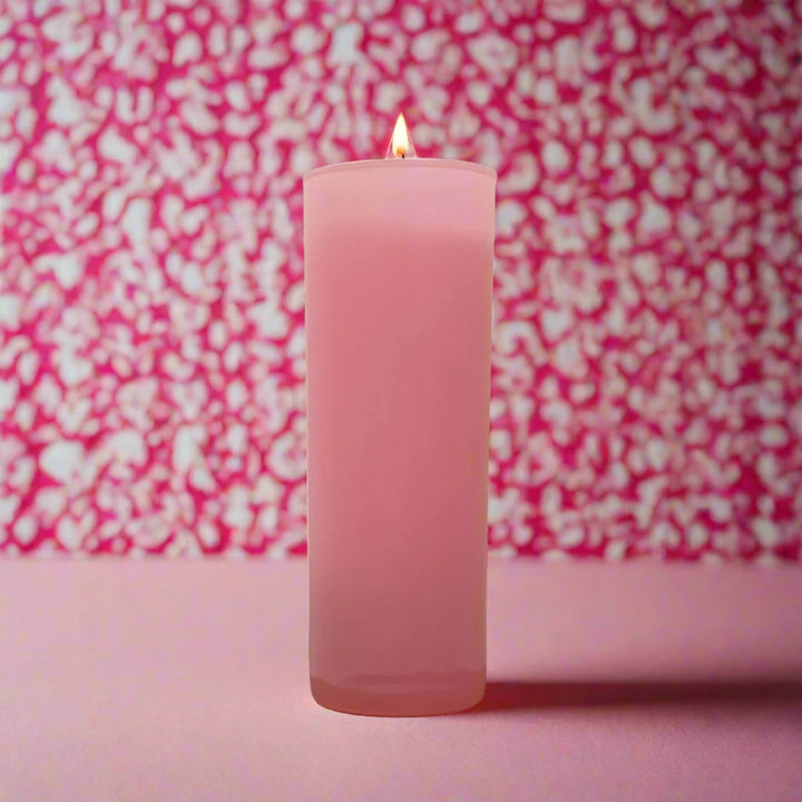 Photograph of a tall pink candle in a frosted glass holder featuring a tiny glowing flame set against a vibrant pink and white leopard-print bokeh background