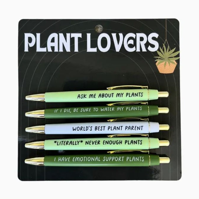 Product photography of five Plant Lovers collection pens in shades of mint, forest green, and white arranged on a black backing card featuring a hanging plant illustration and gold-toned metal accents with humorous slogans like World's Best Plant Parent and Literally Never Enough Plants