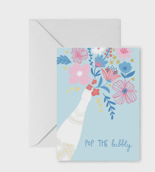 Illustration of a celebratory greeting card featuring a white champagne bottle with gold star details and a vibrant bouquet of pink and blue flowers bursting from the top against a light blue background with the handwritten phrase POP THE bubbly