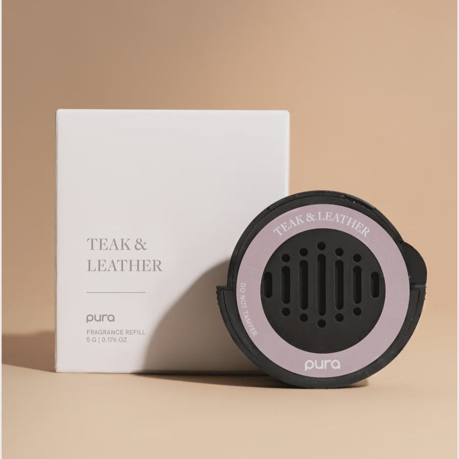 Studio photograph by Pura of a Teak & Leather fragrance refill and its white square packaging box set against a beige background showcasing a circular black diffuser disk with a light purple border and vertical ventilation slits