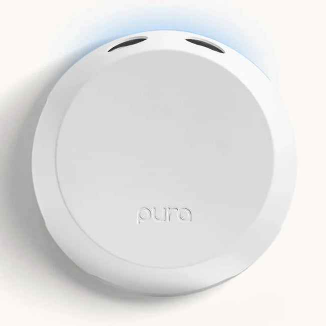 Digital product photograph of a Pura smart home fragrance diffuser on a neutral background featuring a sleek circular white design with an embossed logo, dual top vents, and a soft blue backlighting effect