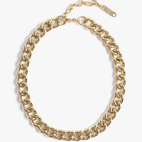 Gold-toned metal curb link necklace featuring thick polished links, an adjustable extender chain with a small rectangular logo tag, and a lobster claw clasp against a minimalist white background