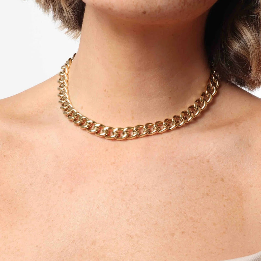 Fashion photograph of a thick gold cuban link necklace worn as a choker featuring high-shine polished surfaces and heavy interlocking links