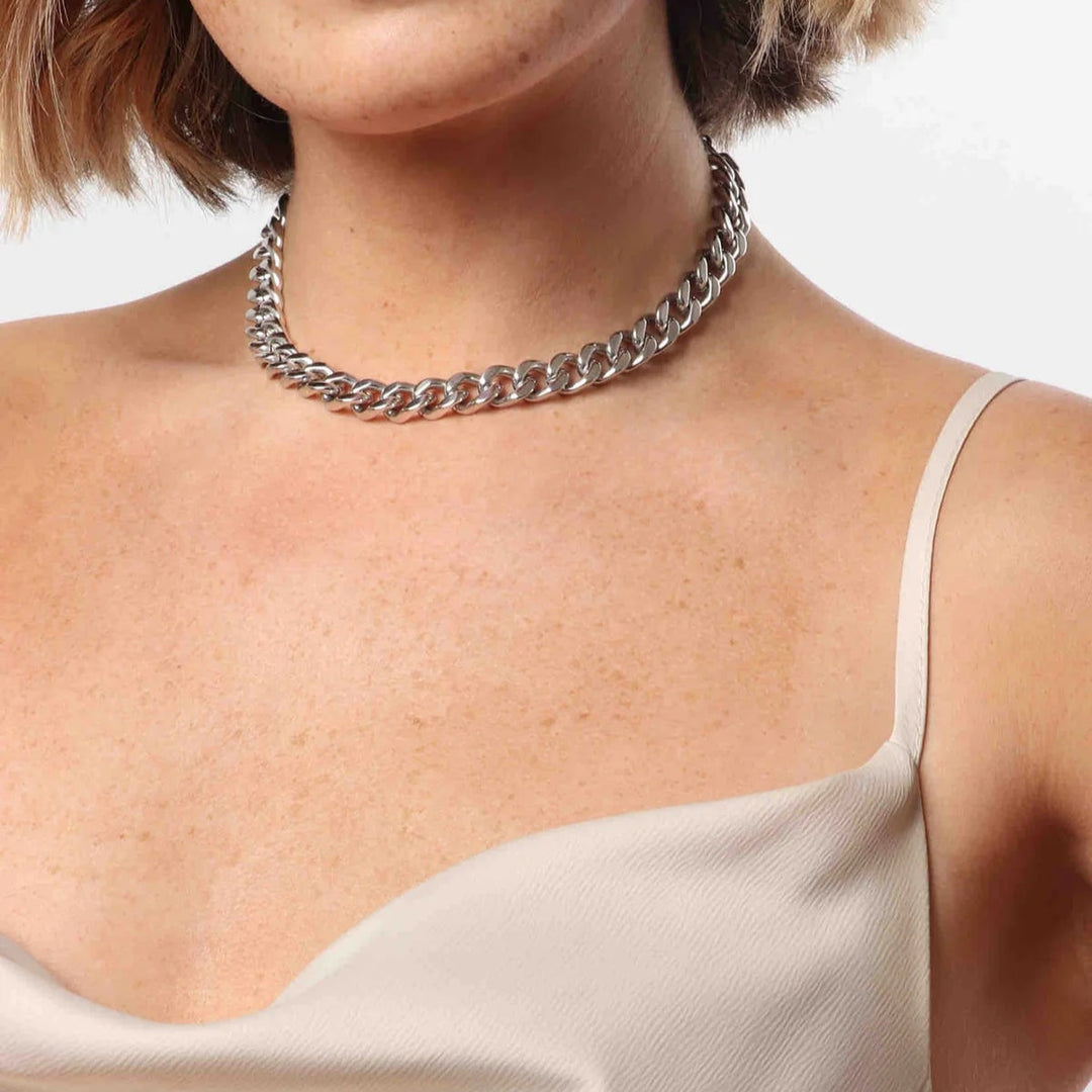 Photograph of a silver cuban link necklace worn by a woman in a studio featuring polished interlocking links, freckled skin, and a cream-colored satin neckline