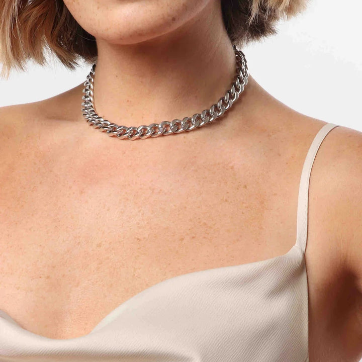 Photograph of a silver cuban link necklace worn by a woman in a studio featuring polished interlocking links, freckled skin, and a cream-colored satin neckline