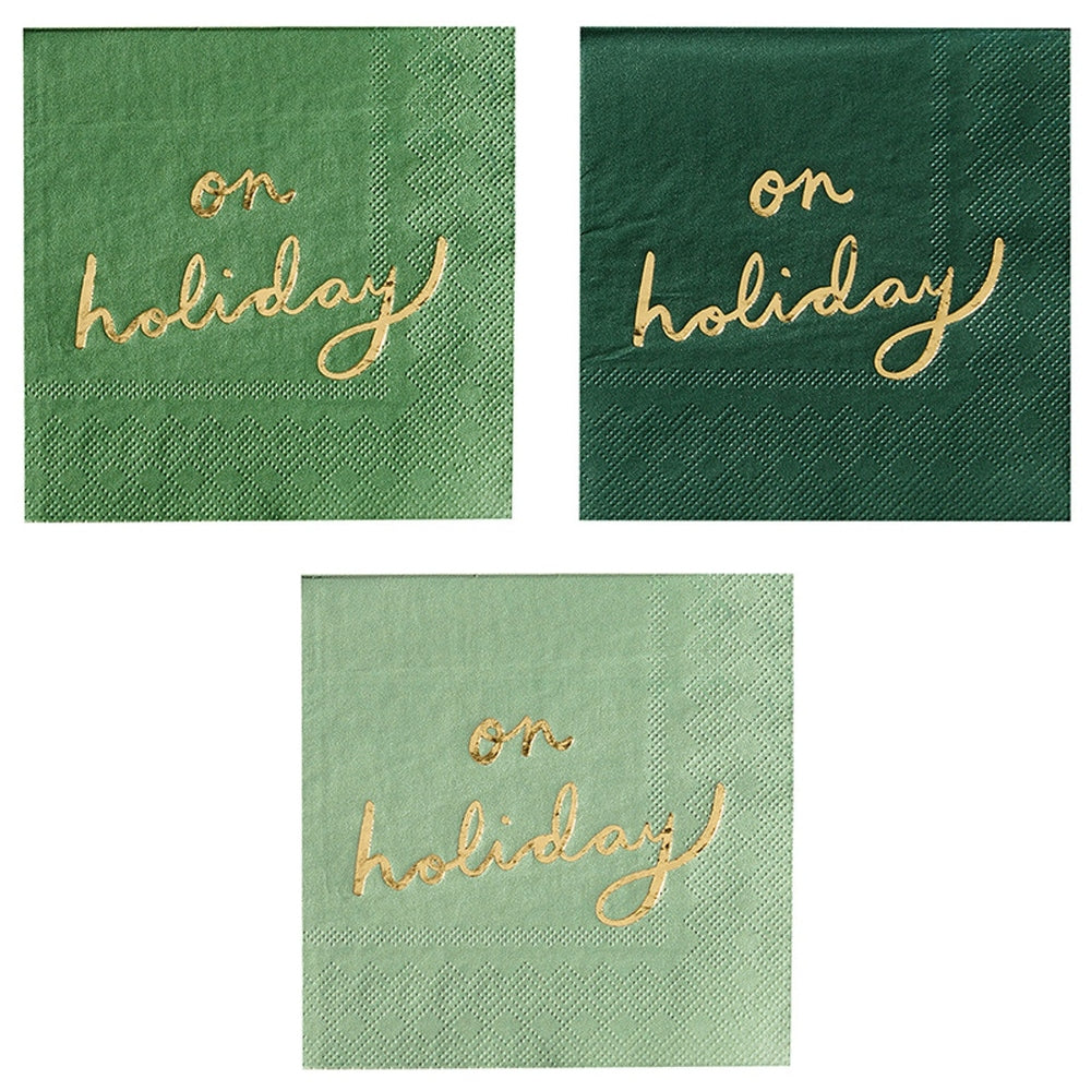 Paper cocktail napkins featuring gold foil cursive lettering reading on holiday in three distinct shades of green including sage and forest with decorative embossed diamond border patterns