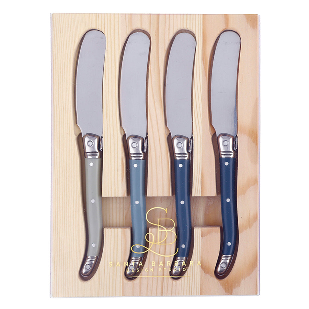 Stainless steel spreader knives by Santa Barbara Design Studio displayed in a light pine wood tray featuring four iconic Laguiole-style handles in a gradient of slate grey and navy blue with polished silver rivets and a gold logo