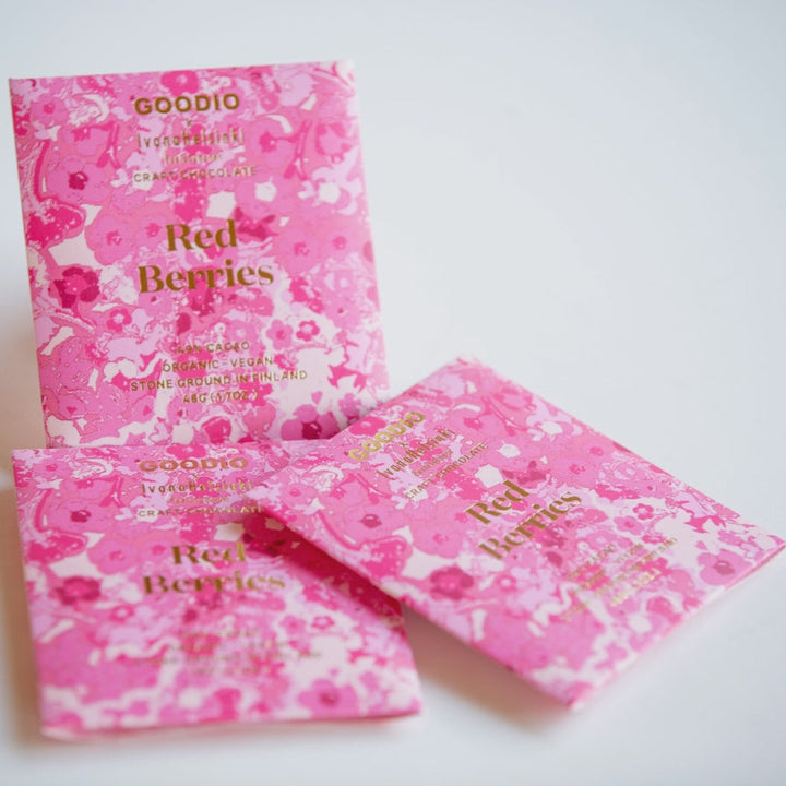 Product photography of Goodio craft chocolate designed by Ivana Helsinki featuring three Red Berries bars with a vibrant pink floral pattern and gold lettering on a white background