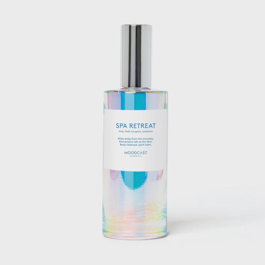 Studio photograph by Moodcast Fragrance Co of the Spa Retreat room spray bottle centered against a light gray backdrop featuring a shimmering iridescent glass finish, a polished silver cap, and a white label with colorful teal and purple abstract strokes