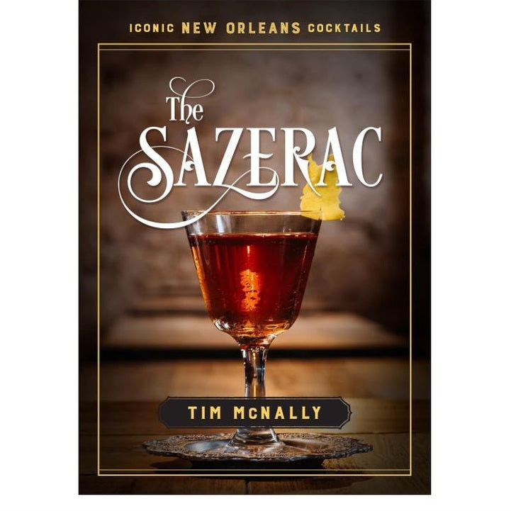 Book cover by Tim McNally featuring the iconic New Orleans Sazerac cocktail shown as a rich amber liquid with a bright yellow lemon twist garnish and an ornate silver coaster on a rustic wooden table