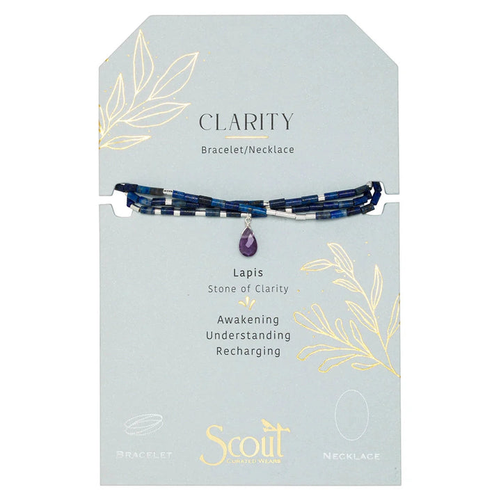 Commercial product photography by Scout Curated Wears showcasing a Lapis Stone of Clarity convertible bracelet and necklace on a light blue card featuring gold foil botanical drawings, deep blue lapis tube beads, and a central faceted purple amethyst teardrop pendant