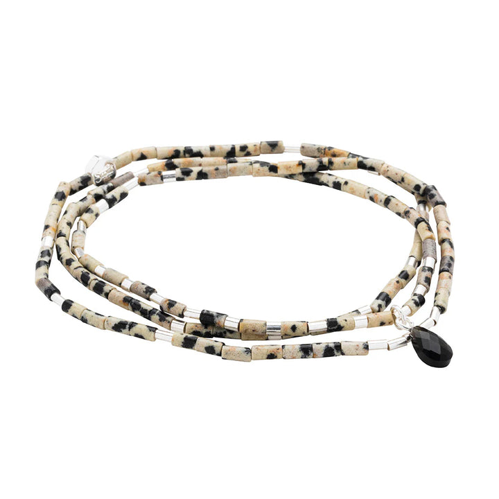 Handmade dalmatian jasper multi-wrap bracelet by Scout Curated Wear featuring cylindrical spotted beige beads, shimmering silver spacers, and a single faceted black teardrop charm on a white background