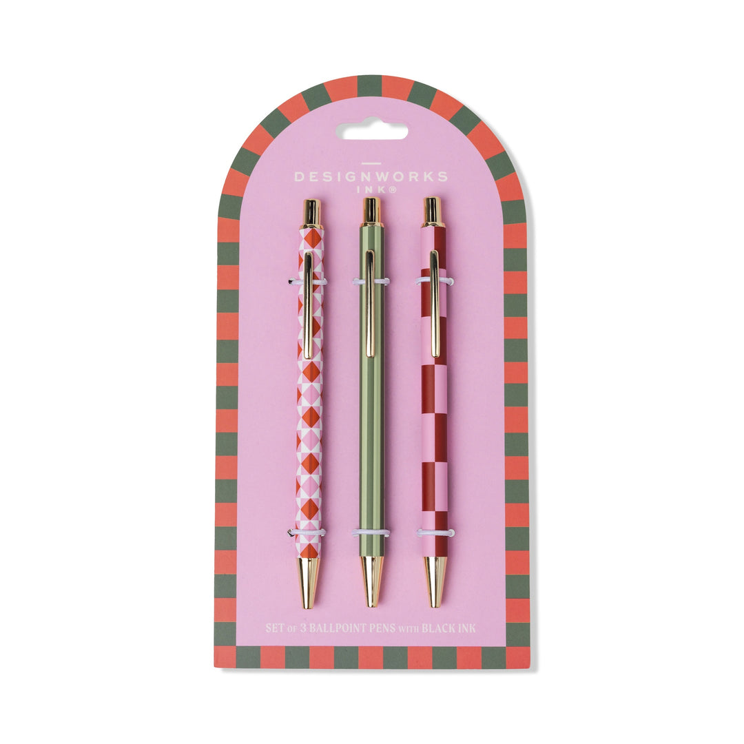 Set of three ballpoint pens by Designworks Ink featuring red and pink harlequin, green striped, and checkerboard patterns on a pink arched card with a red and green checkered border and gold hardware