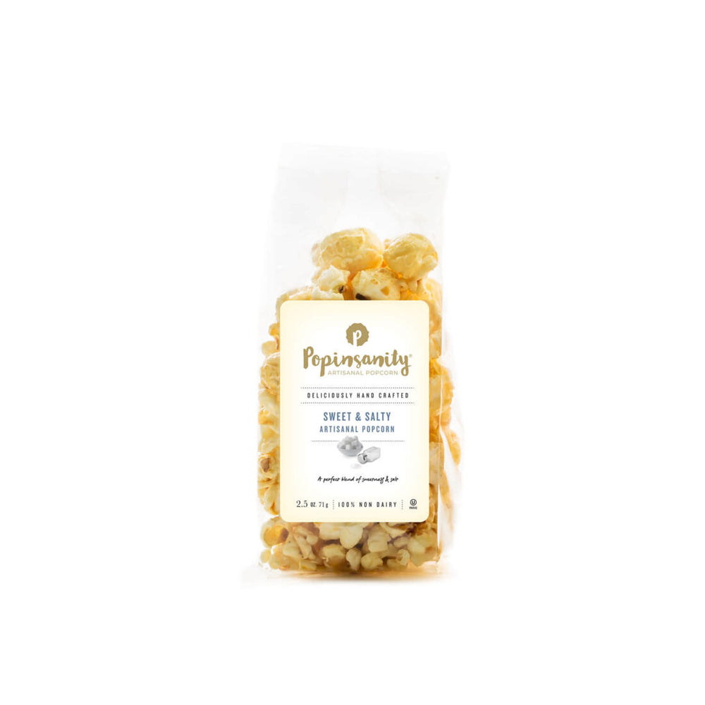 Studio product photograph by Popinsanity of a clear bag of Sweet and Salty artisanal popcorn on a white background, featuring large golden-glazed kernels and a cream label with the signature P logo and elegant gold-toned typography