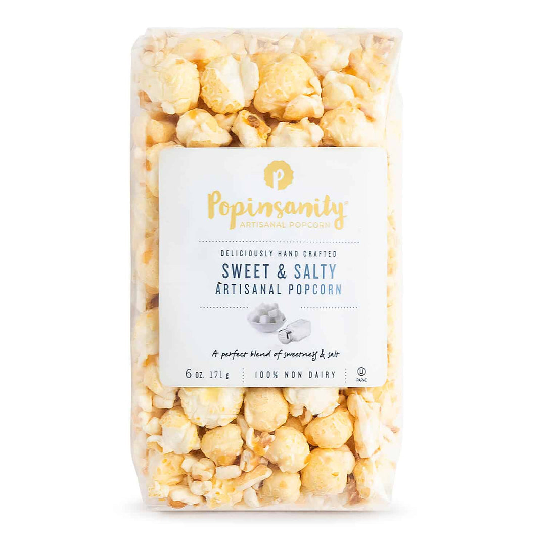Commercial product photograph by Popinsanity of a clear bag of Sweet & Salty Artisanal Popcorn on a white studio background featuring large golden kernels, a signature gold P logo, and blue serif typography