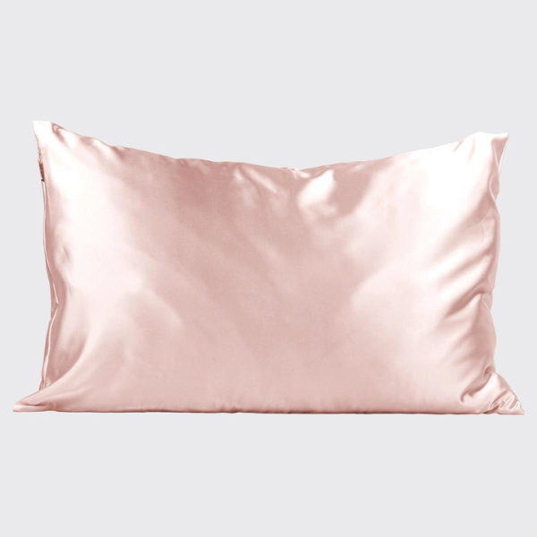 Studio photography of a blush pink silk pillowcase featuring a lustrous satin sheen and soft fabric folds against a plain light gray background