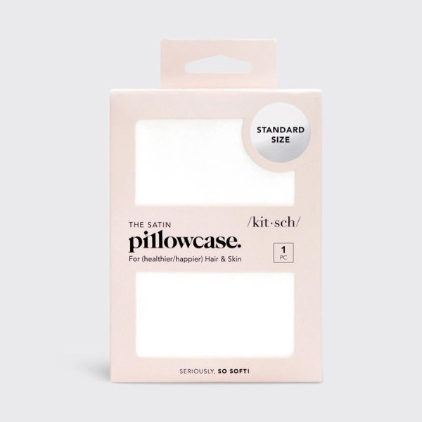 Digital product photography by Kitsch featuring a white satin pillowcase in blush pink retail packaging that highlights the brand logo, a silver circular standard size sticker, and rectangular window cut-outs showing the glossy fabric texture against a light grey backdrop