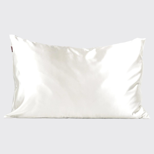 Product photograph of a white silk pillowcase centered on a plain grey studio background featuring a lustrous satin sheen, smooth surface ripples, and a small red brand label on the left edge