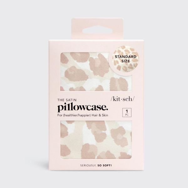 Product photography by Kitsch of a leopard print satin pillowcase in a blush pink retail box featuring a neutral tan animal pattern, the Kitsch brand logo, and bold black typography highlighting hair and skin benefits
