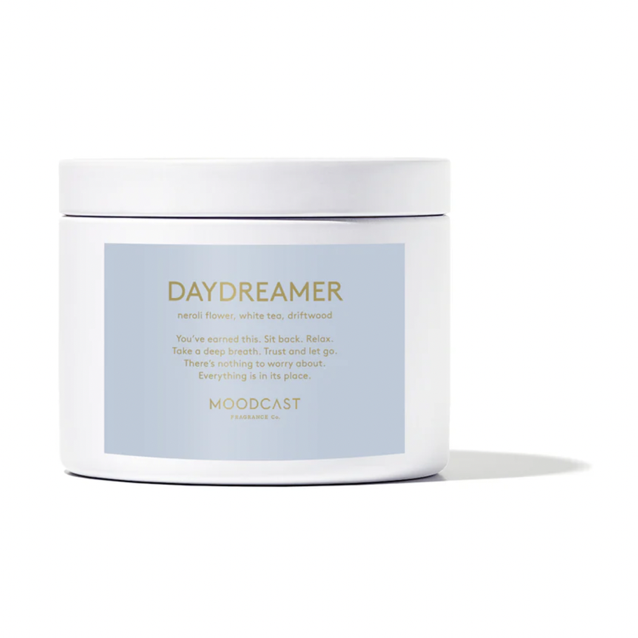 Studio photograph of a Moodcast Fragrance Co. Daydreamer candle featuring a white ceramic jar with a light blue label and gold metallic lettering listing notes of neroli flower and white tea against a white background