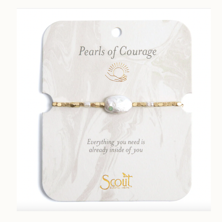 Jewelry by Scout Curated Wears featuring a Pearls of Courage bracelet on a marble-patterned card with a gold sun icon, a large irregular baroque pearl with a tiny green gemstone, and faceted gold-tone beads