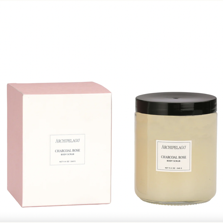 Product photograph of Archipelago Charcoal Rose Body Scrub featuring a minimalist white and pastel pink box beside a clear glass jar with a glossy black lid and cream-colored contents against a neutral white background