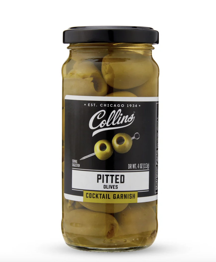 Studio photograph of a Collins brand jar of pitted olives featuring large green olives in clear brine, a black lid, and a black label with an iconic Chicago 1934 established mark and a yellow cocktail garnish strip