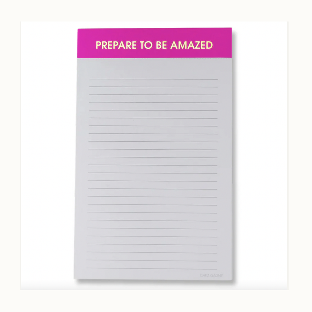 Stationery by Chez Gagné featuring a centered lined notepad with a vibrant hot pink header containing the gold-lettered phrase PREPARE TO BE AMAZED and thin gray horizontal lines on a light background
