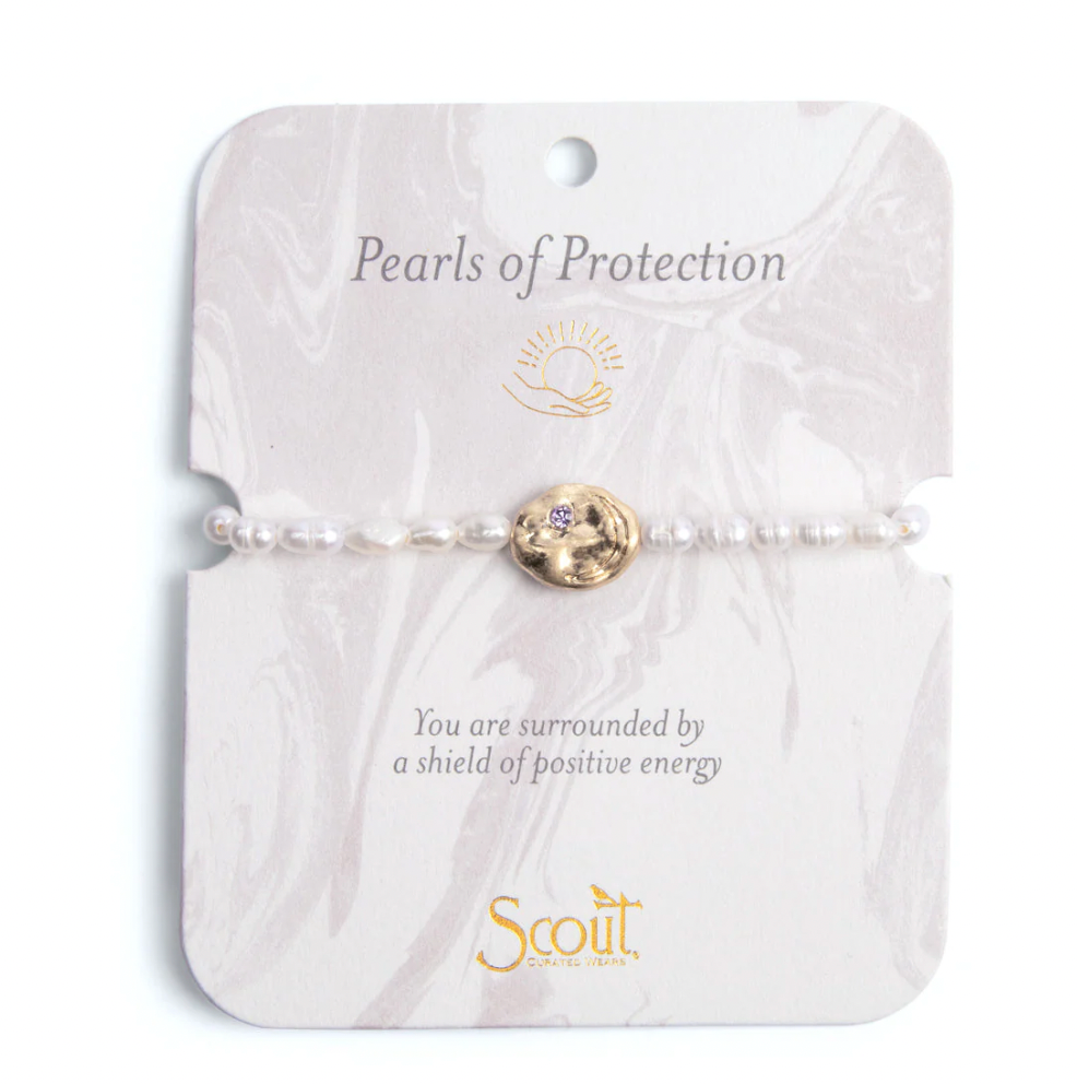 Jewelry by Scout Curated Wears featuring a Pearls of Protection bracelet with dainty white pearls and a hammered gold medallion inset with a purple crystal displayed on a marble-textured card with gold foil script