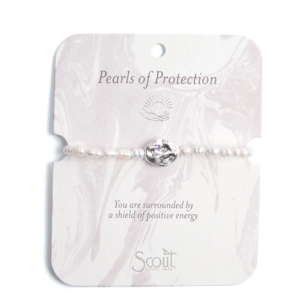 Jewelry photography by Scout Curated Wear of a Pearls of Protection bracelet featuring small white freshwater pearls and a central hammered silver charm with a tiny purple crystal on a light pink marbled display card featuring the brand logo at the bottom