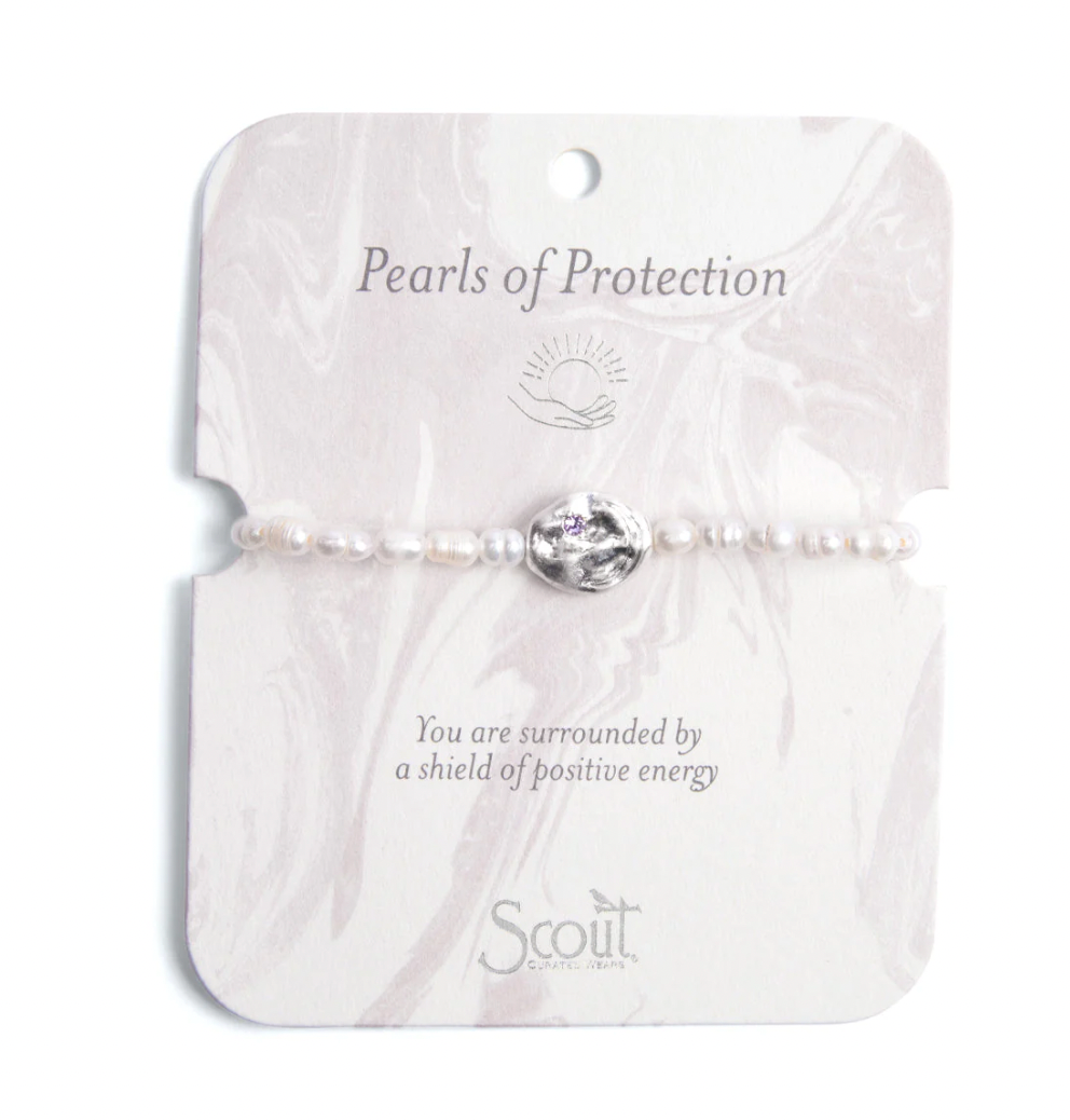 Jewelry by Scout Curated Wear featuring a delicate bracelet of small white pearls centered on a marble-patterned display card with a hammered silver charm inset with a tiny purple crystal and the text Pearls of Protection