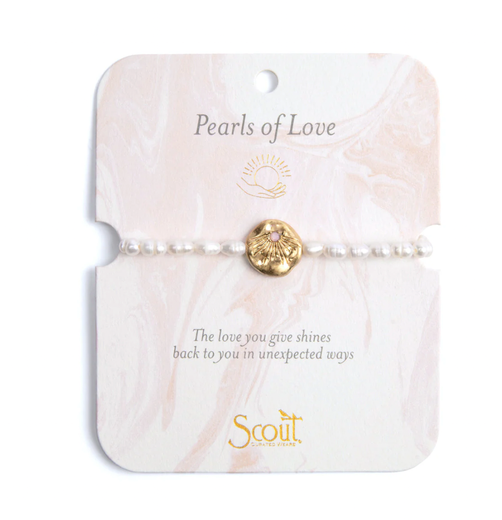 Pearl bracelet by Scout Curated Wears featuring a row of shimmering white rice pearls and a hammered gold sunburst charm with a pink center on a pink marbled display card with the brand&