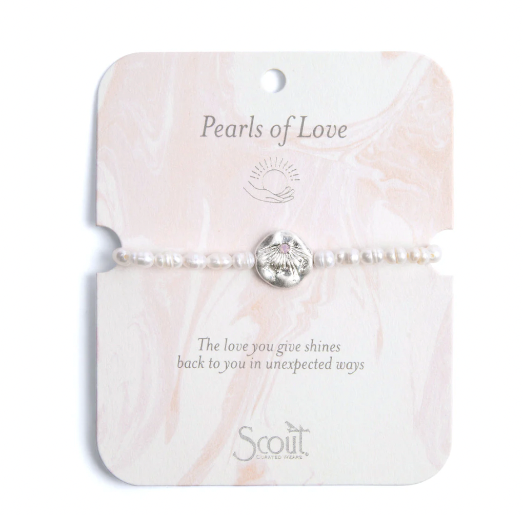 Jewelry by Scout Curated Wears featuring a Pearls of Love bracelet with white freshwater pearls and a hammered silver sunburst charm with a pink center stone on a pink marble-patterned display card with the brand logo and inspirational text