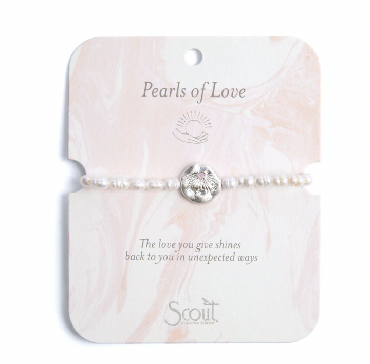 Jewelry by Scout Curated Wears featuring a Pearls of Love bracelet with white freshwater pearls and a hammered silver sunburst charm with a pink center stone on a pink marble-patterned display card with the brand logo and inspirational text
