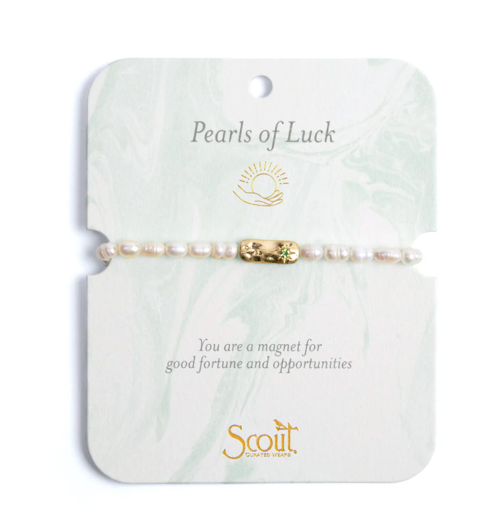 Jewelry by Scout Curated Wears featuring a pearl bracelet with a gold bar charm and a green gemstone on a pale green marbled card with the Pearls of Luck title and gold sun logo