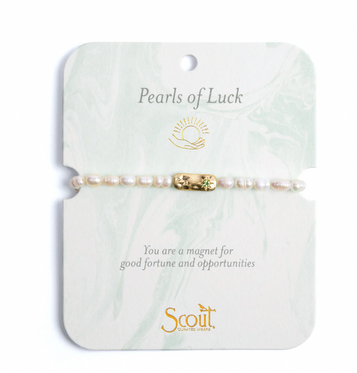 Jewelry by Scout Curated Wears featuring a pearl bracelet with a gold bar charm and a green gemstone on a pale green marbled card with the Pearls of Luck title and gold sun logo