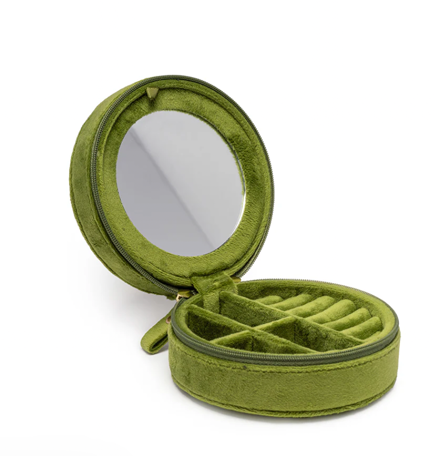 Studio photograph of a plush moss green velvet circular jewelry travel case featuring a built-in round mirror, multiple soft ring rolls, and divided internal compartments against a white background