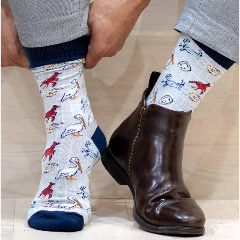 Photograph of light blue novelty socks featuring red lobsters and white pelicans paired with a dark brown leather zip-up boot on a light wood surface