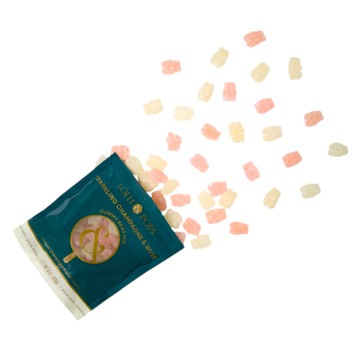 Studio photograph by Lolli & Pops of a teal bag of Sparkling Champagne and Rosé gummy bears spilling across a plain white surface with translucent pink and cream candies and gold foil typography