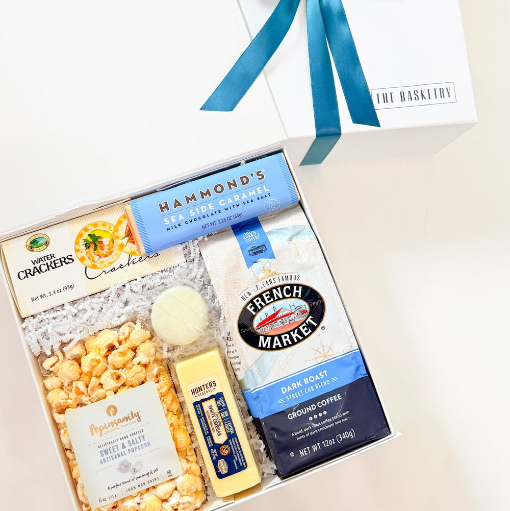 Gift basket with popcorn, crackers, coffee, and other snacks on a light background