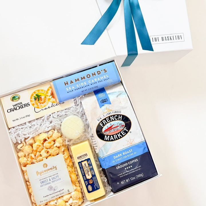 Gift basket with popcorn, crackers, coffee, and other snacks on a light background