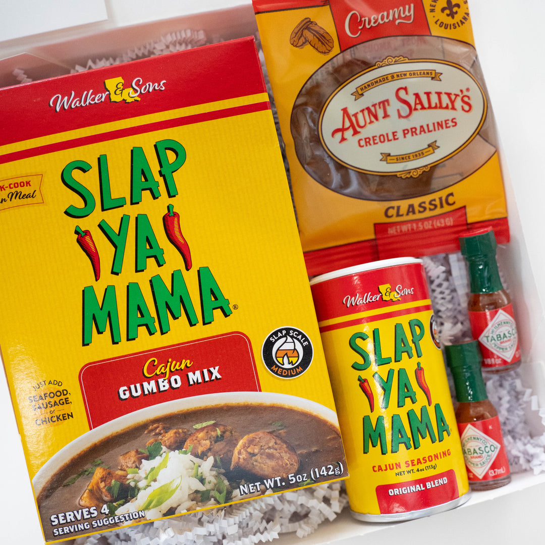 Photograph of a New Orleans food gift box featuring vibrant yellow Slap Ya Mama packaging with red chili pepper graphics, Aunt Sally&